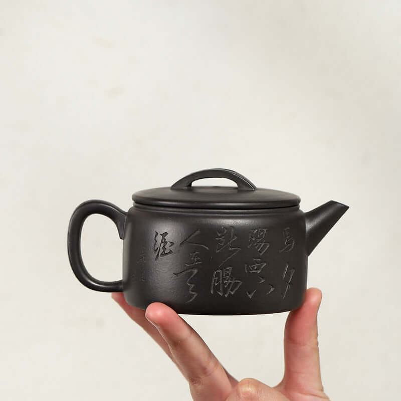 Handmade Yixing purple sand teapot held by a hand, featuring beautiful engravings and a classic design.