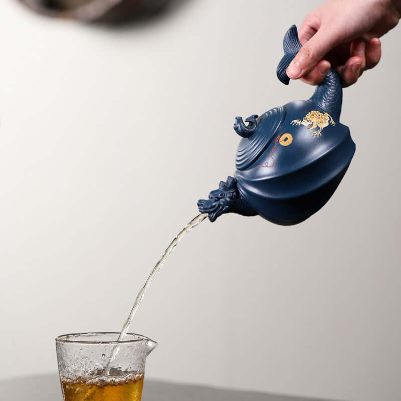 Handmade Yixing purple sand teapot pouring tea into a glass, showcasing intricate design and craftsmanship.