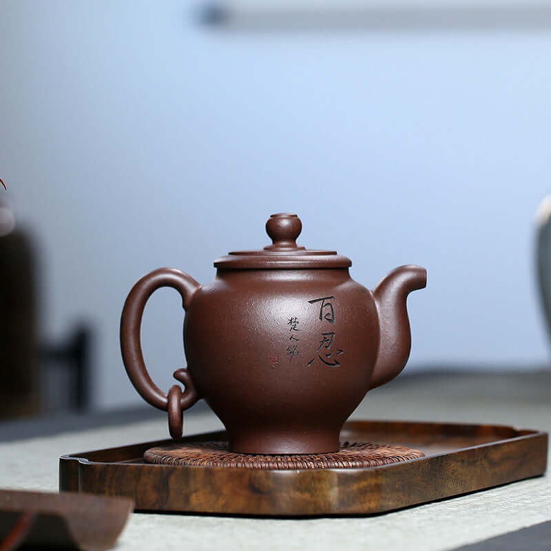 Handmade Yixing purple sand teapot with elegant engraving, displayed on a wooden tray for traditional Kung Fu tea.