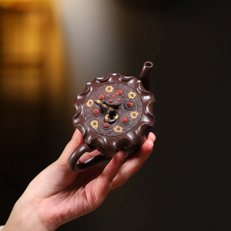 Handmade Yixing purple sand teapot featuring a floral design, held by a hand, showcasing its unique craftsmanship.