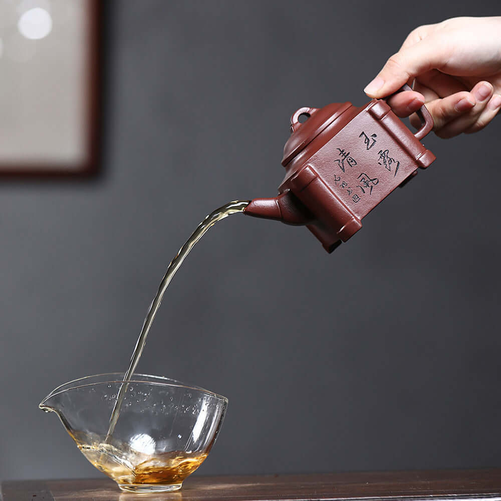 Handmade Yixing purple sand teapot pouring tea into a glass bowl, showcasing traditional Kung Fu tea set craftsmanship.