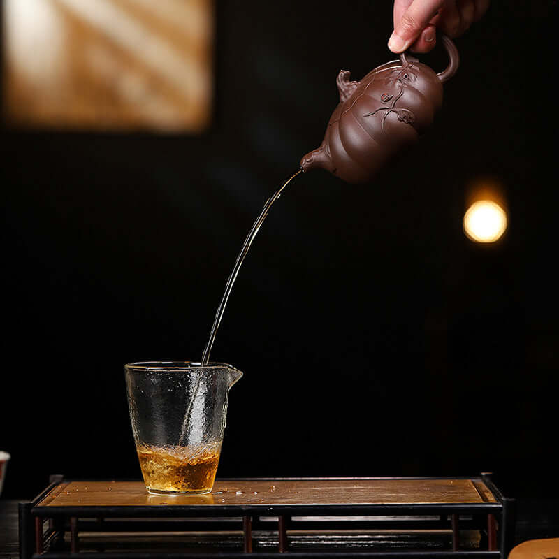Handmade Yixing purple sand teapot pouring tea into a glass, showcasing elegant craftsmanship and functionality.