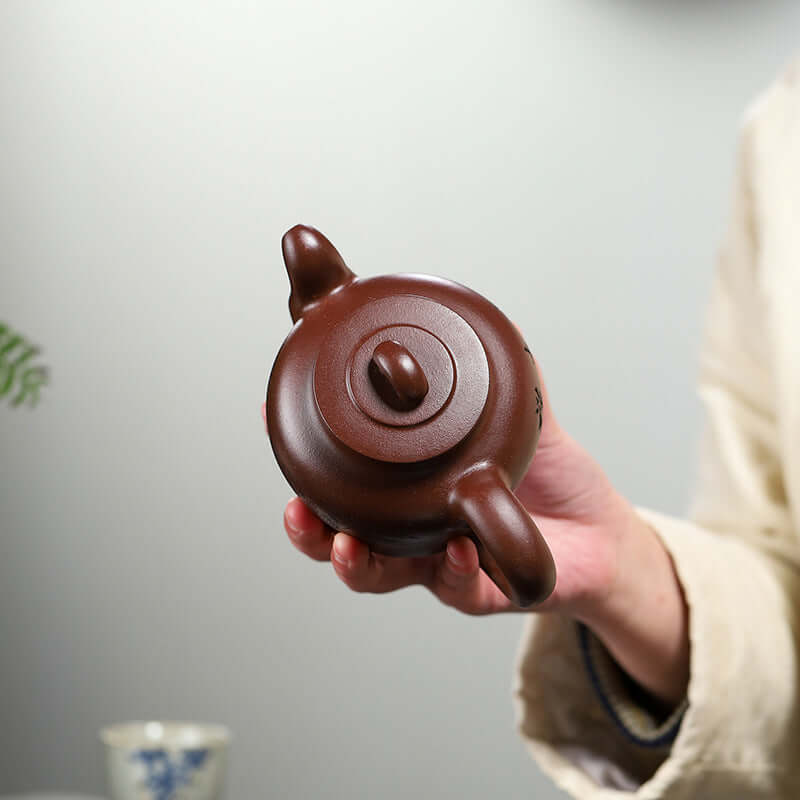 Handmade Yixing purple sand teapot held from above, featuring a round body and a smooth lid.