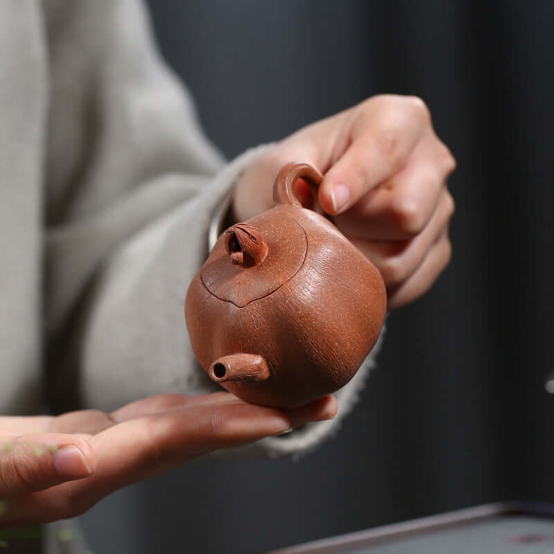 Handmade Yixing purple sand teapot held in hand, showcasing exquisite craftsmanship and unique design.