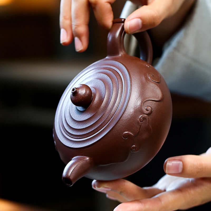 Handmade Yixing purple sand teapot held by a craftsman, showcasing elegant design and unique features.
