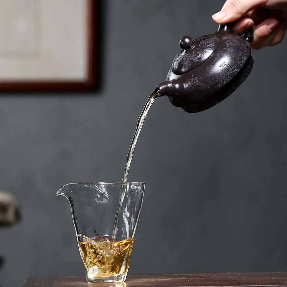Handmade Yixing purple sand teapot pouring tea into a glass, showcasing fine craftsmanship and traditional kung fu tea set.