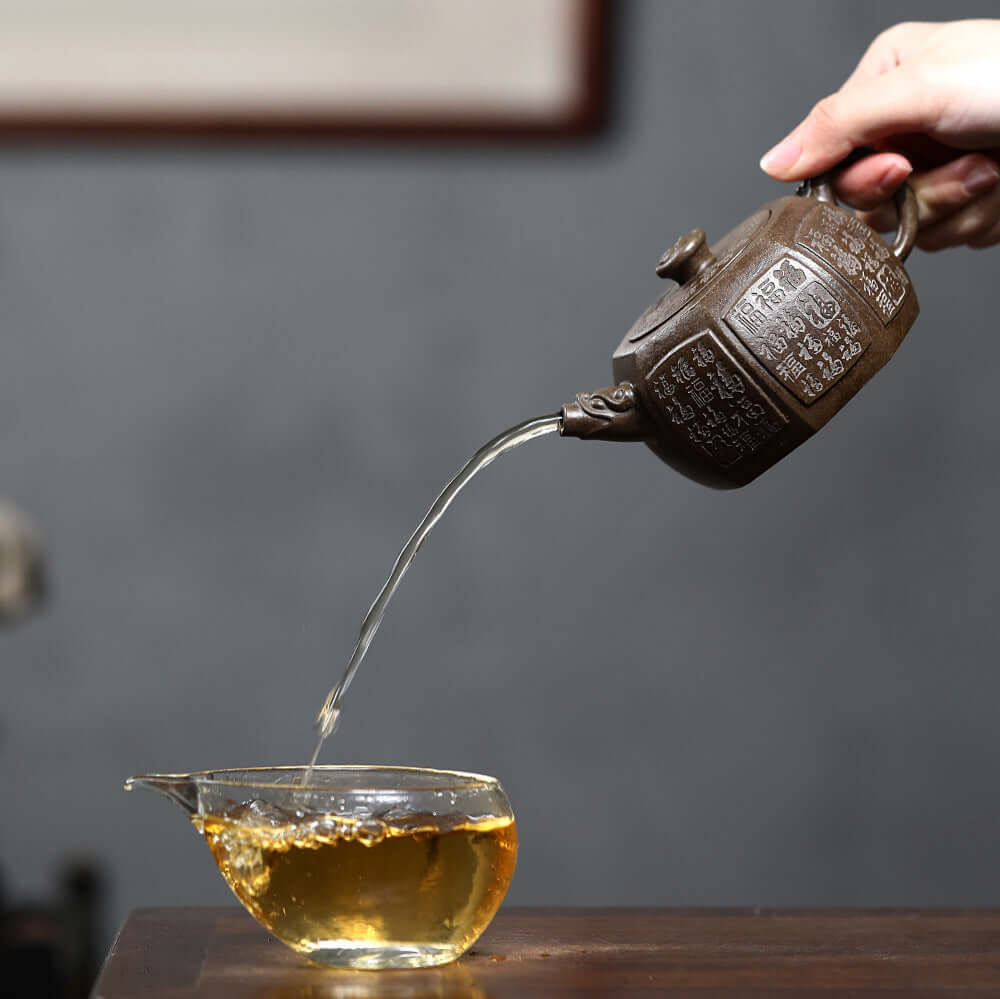Handmade Yixing purple sand teapot pouring tea into a glass cup, showcasing craftsmanship and traditional tea culture.