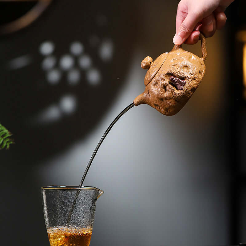 Handmade Yixing purple sand teapot pouring tea into a glass, showcasing unique craftsmanship and design.