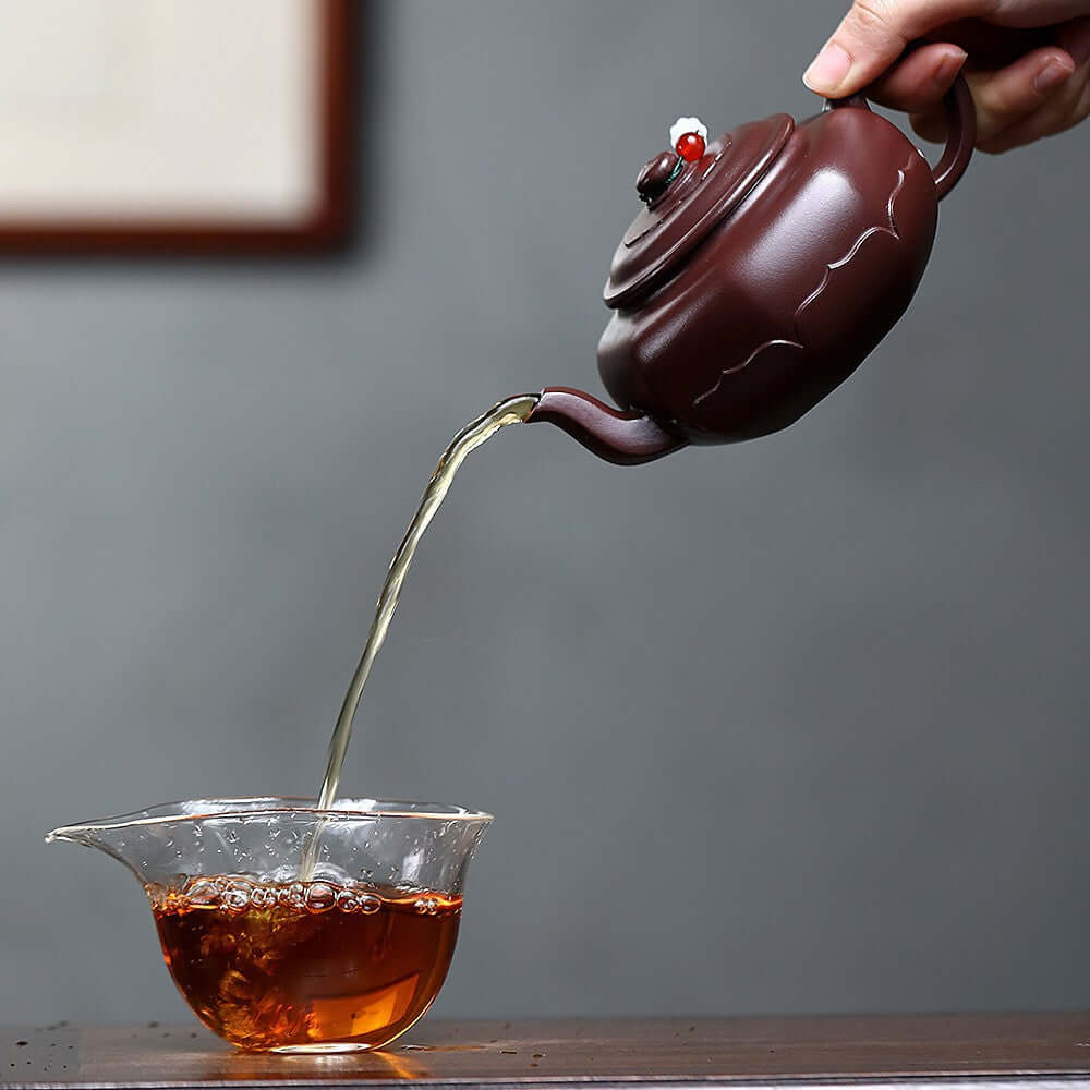 Handmade Yixing purple sand teapot pouring tea into glass cup, showcasing traditional kung fu tea set craftsmanship.