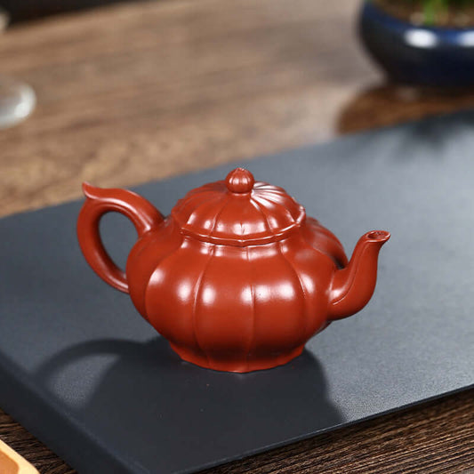 Handmade Yixing purple sand teapot with a pumpkin shape, showcasing intricate design and vibrant red color.