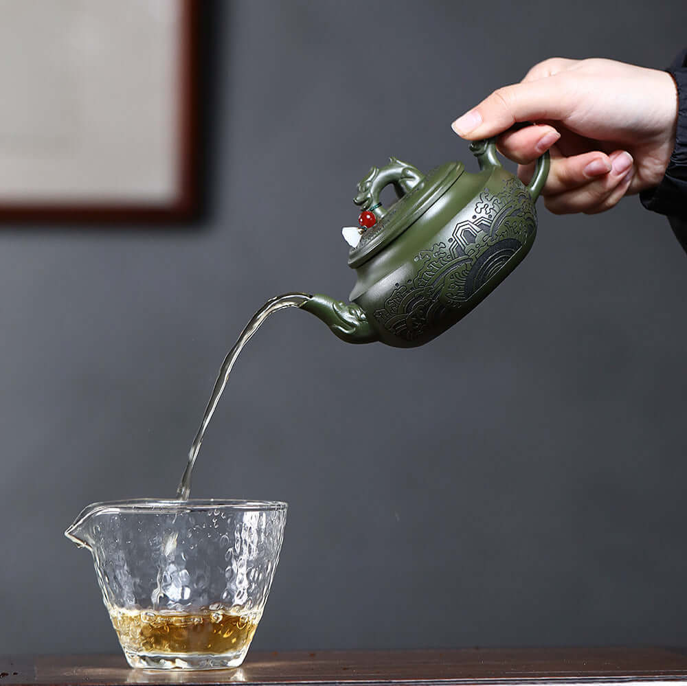 Handmade Yixing purple sand teapot pouring tea into a glass cup, showcasing elegant craftsmanship and design.