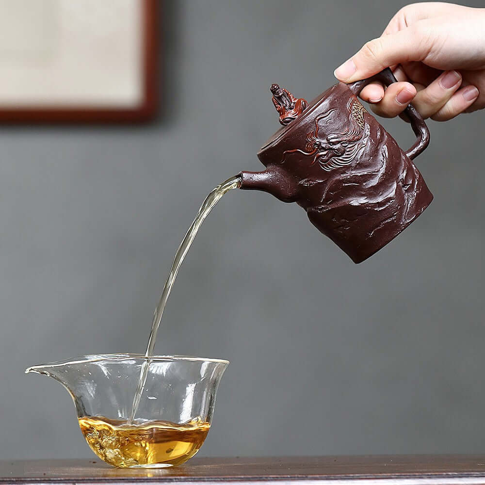 Handmade Yixing purple sand teapot pouring tea into a glass cup, showcasing traditional Kung Fu tea set craftsmanship.