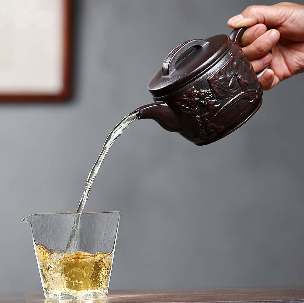 Handmade Yixing purple sand teapot pouring tea into a glass, showcasing craft design and quality.