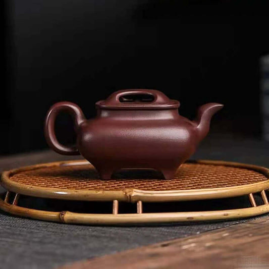 Handmade Yixing purple sand teapot resting on a bamboo tray, showcasing artisanal craftsmanship.