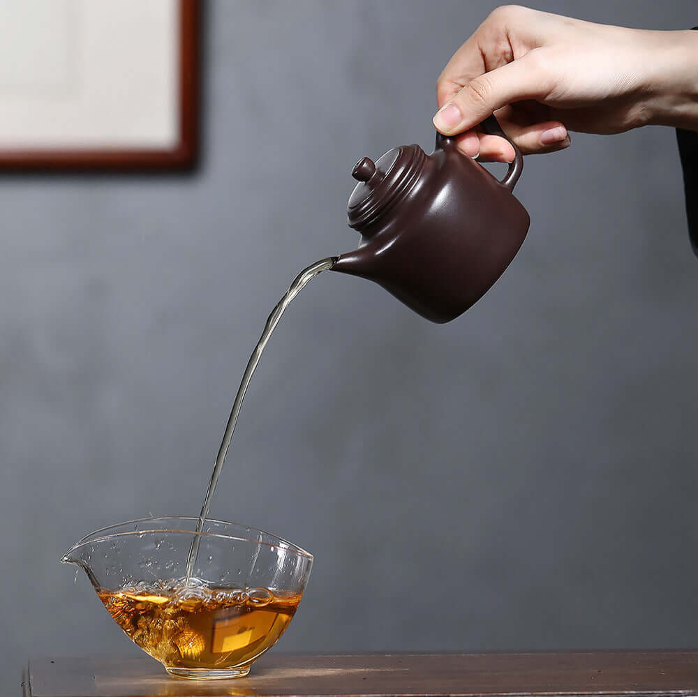 Handmade Yixing purple sand teapot pouring tea into a glass cup, showcasing traditional Kung Fu tea style.
