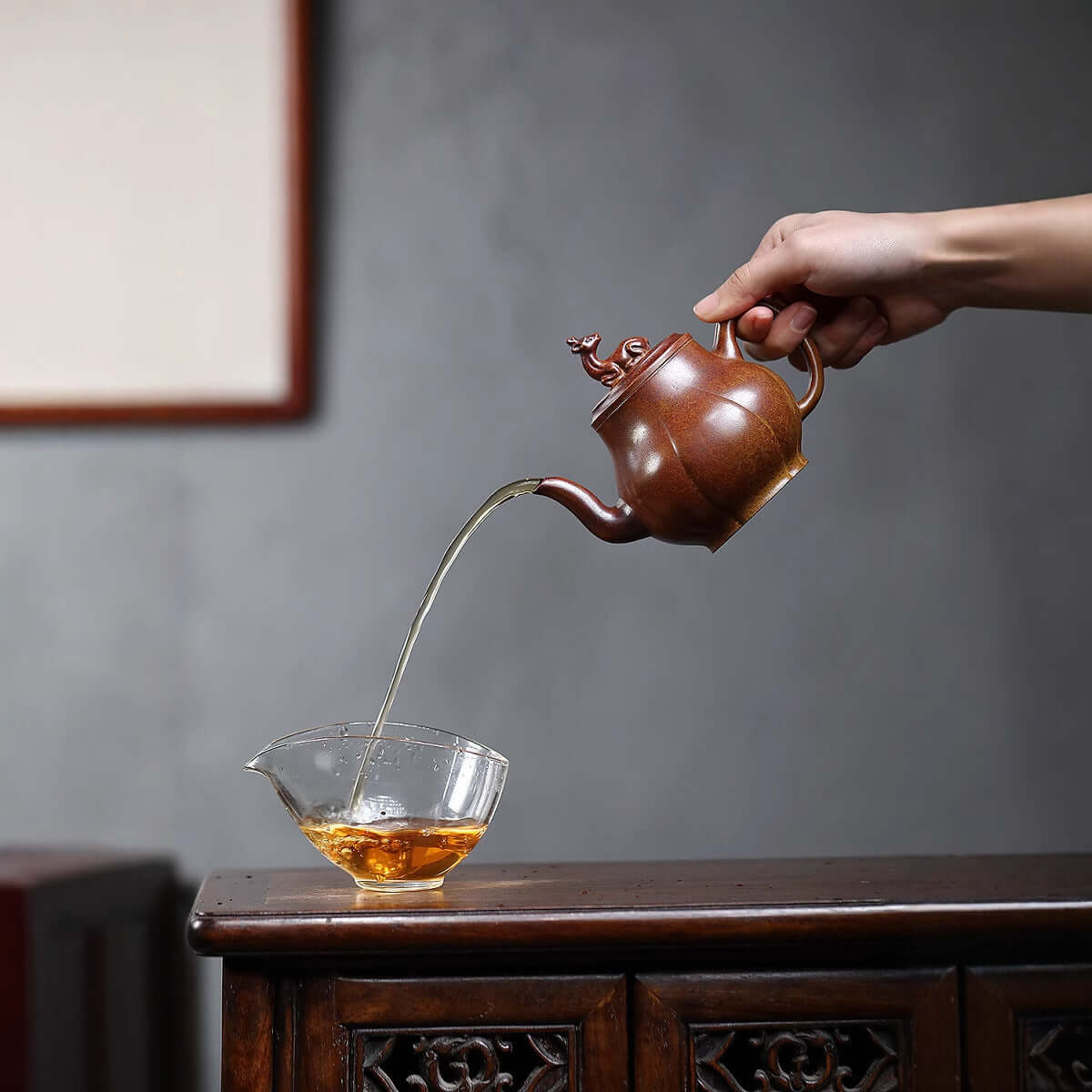 Handmade Yixing purple sand teapot pouring tea into a glass cup, showcasing elegant craftsmanship and ancient techniques.