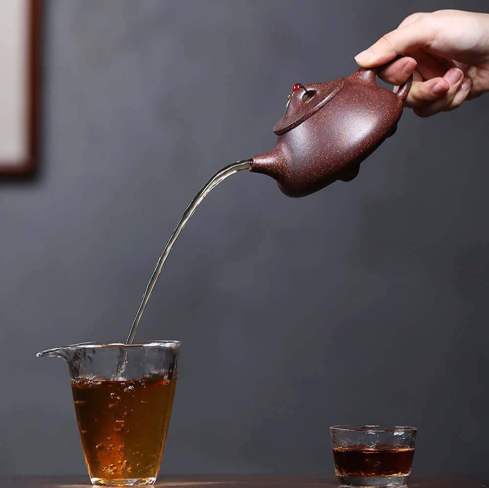 Handmade Yixing purple sand teapot pouring tea, showcasing craftsmanship and elegance in Kung Fu tea preparation.