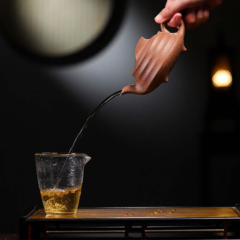 Handmade Yixing purple sand teapot pouring tea into a glass cup for kung fu tea ceremony.