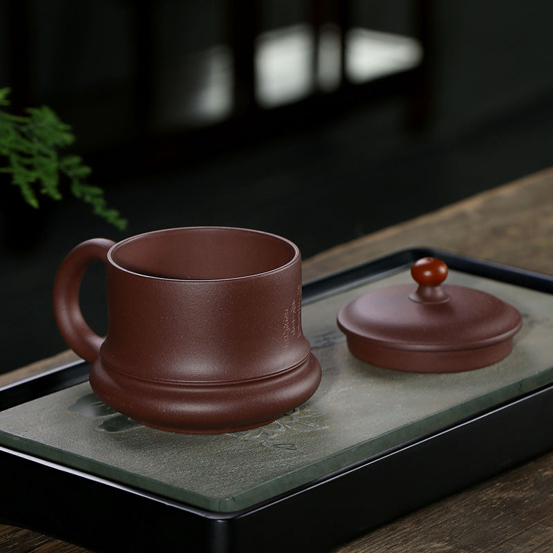 Handmade Yixing purple sand cup with lid, showcasing elegant design on a tea tray.