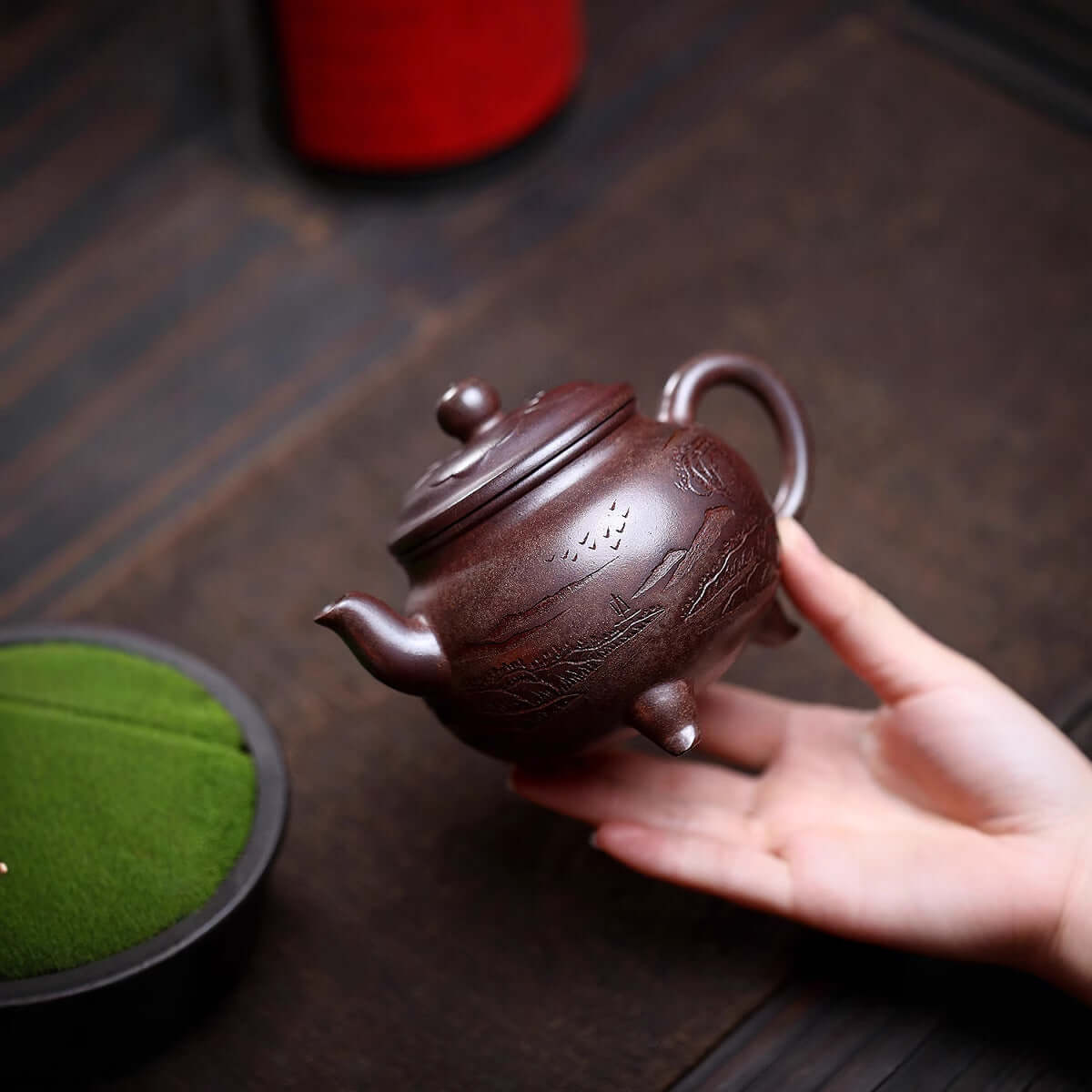 Handmade Yixing purple sand teapot held in hand, showcasing intricate design, perfect for tea lovers.