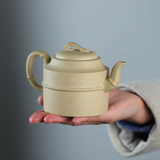 Handmade Yixing purple sand teapot in a person's hand, showcasing intricate design and craftsmanship.