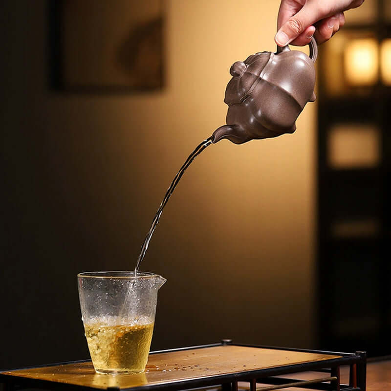 Handmade Yixing purple sand teapot pouring tea into a glass, showcasing traditional craftsmanship and rich tea culture.
