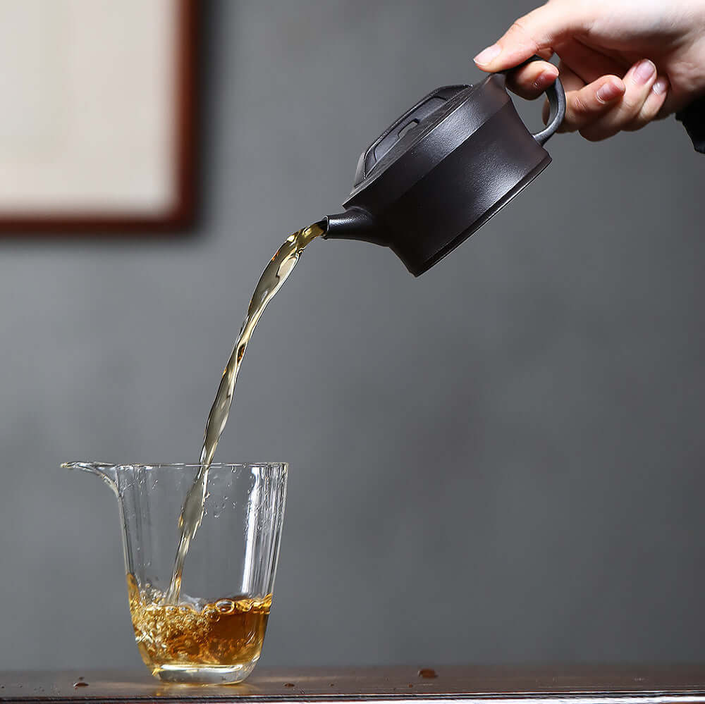 Handmade Yixing purple sand teapot pouring tea into a glass cup, showcasing traditional Kung Fu tea set craftsmanship.