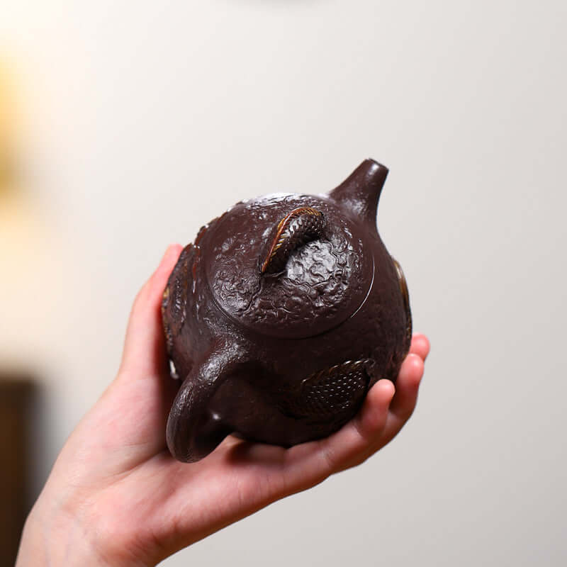 Handcrafted Yixing purple sand teapot featuring traditional relief dragon design, held in hand, showcasing unique craftsmanship.