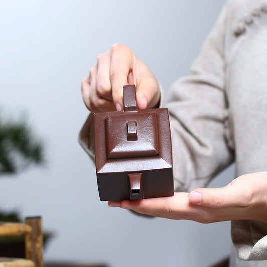 Handmade Yixing purple sand teapot showcased in a person's hands, highlighting its unique square design and craftsmanship.