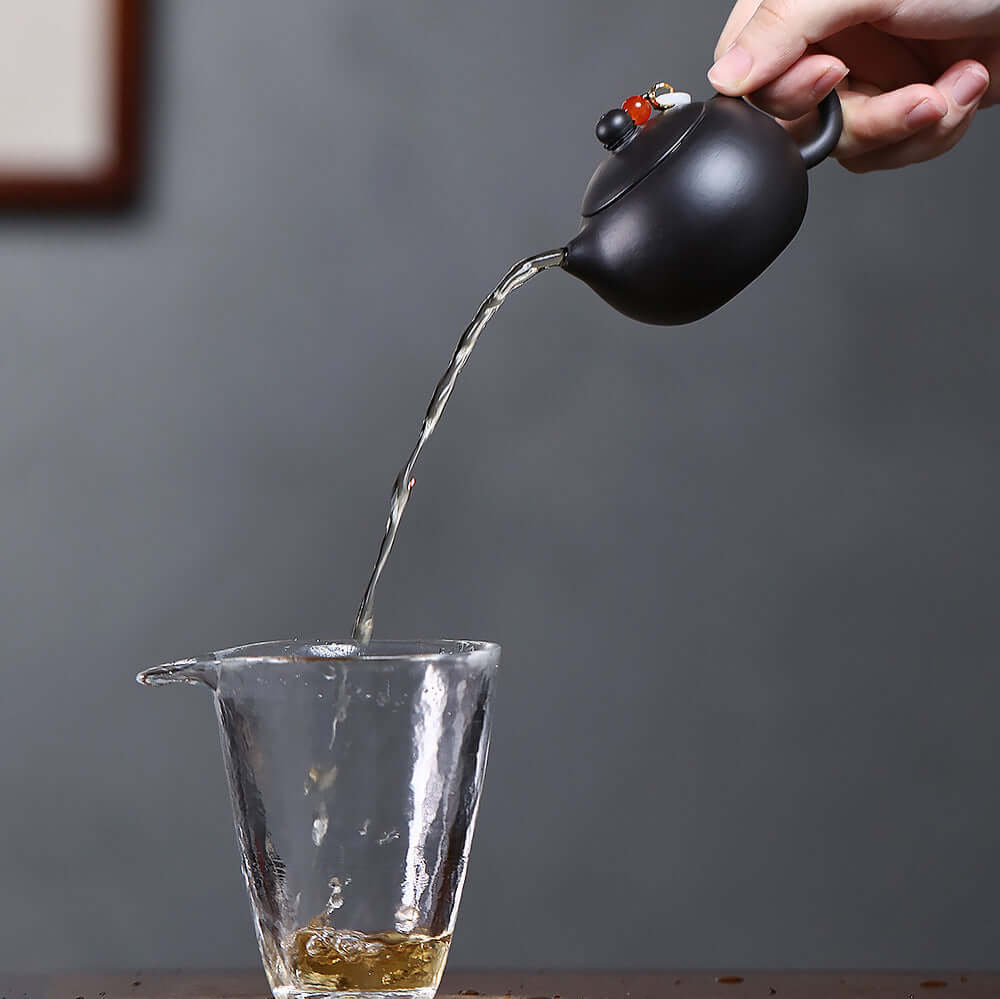 Handmade Yixing purple sand teapot pouring tea into a glass cup, showcasing original craftsmanship in a Kung Fu tea set.