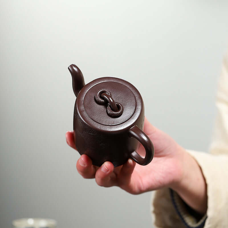 Handmade Yixing purple sand teapot with double rings, showcasing traditional craftsmanship in a hand-held view.
