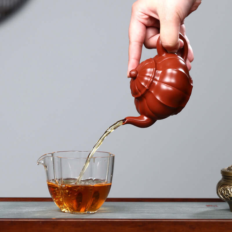 Handmade Yixing purple sand teapot pouring tea into a glass cup, showcasing traditional Kung Fu tea set.