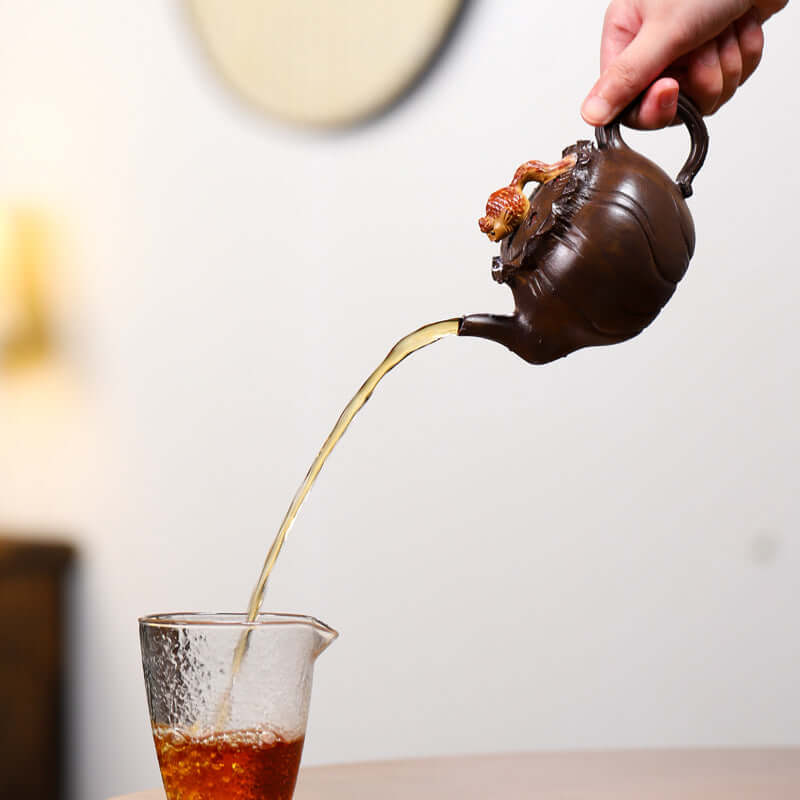 Handmade Yixing purple sand teapot pouring tea into a glass cup, showcasing elegant design and craftsmanship.