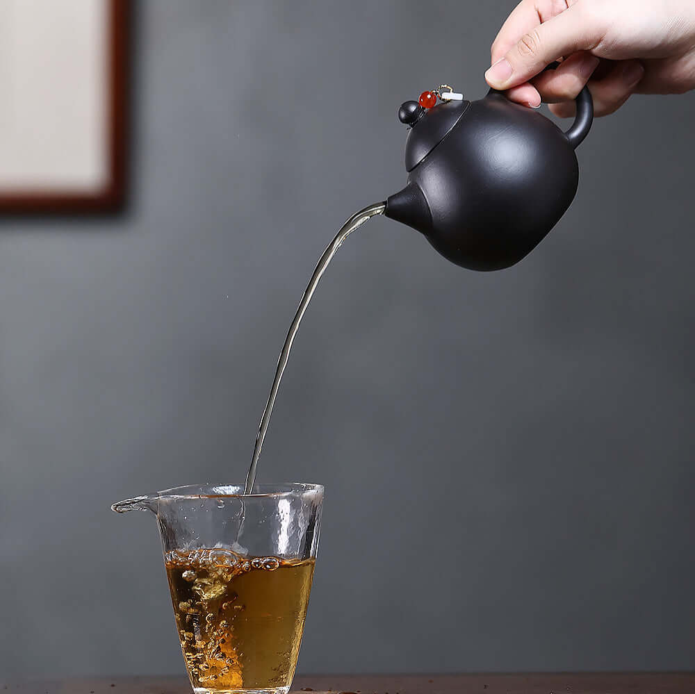 Handmade Yixing purple sand teapot pouring tea into a glass, showcasing craftsmanship in Kung Fu tea practice.