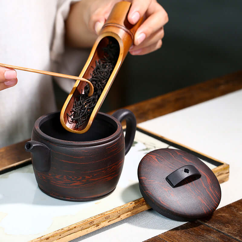 Handcrafted Yixing purple sand teapot with loose tea being added, showcasing traditional Chinese tea culture.