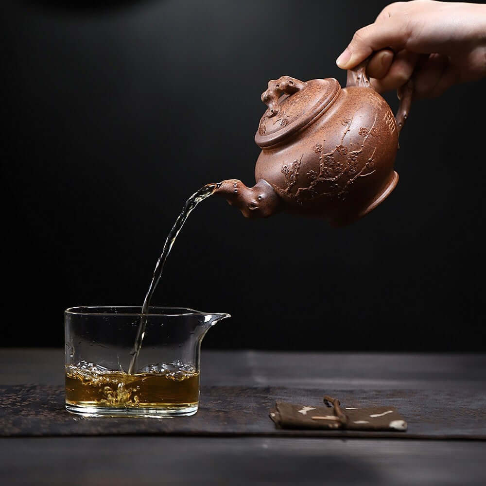 Handmade Yixing purple sand teapot pouring tea into a glass cup, showcasing exquisite craftsmanship and traditional kung fu tea preparation.