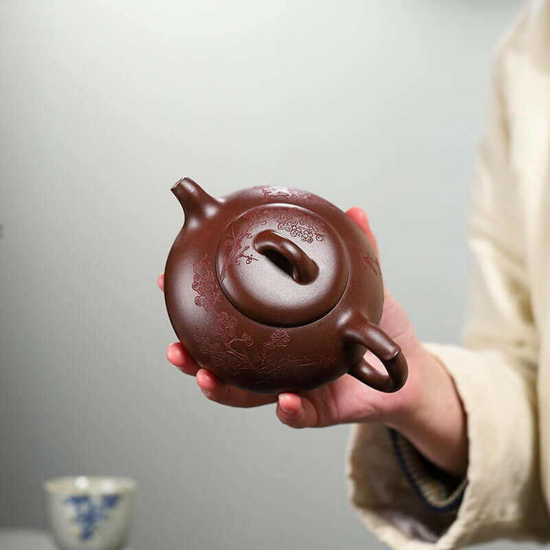 Handmade Yixing purple sand teapot being held, showcasing intricate floral designs and smooth craftsmanship.