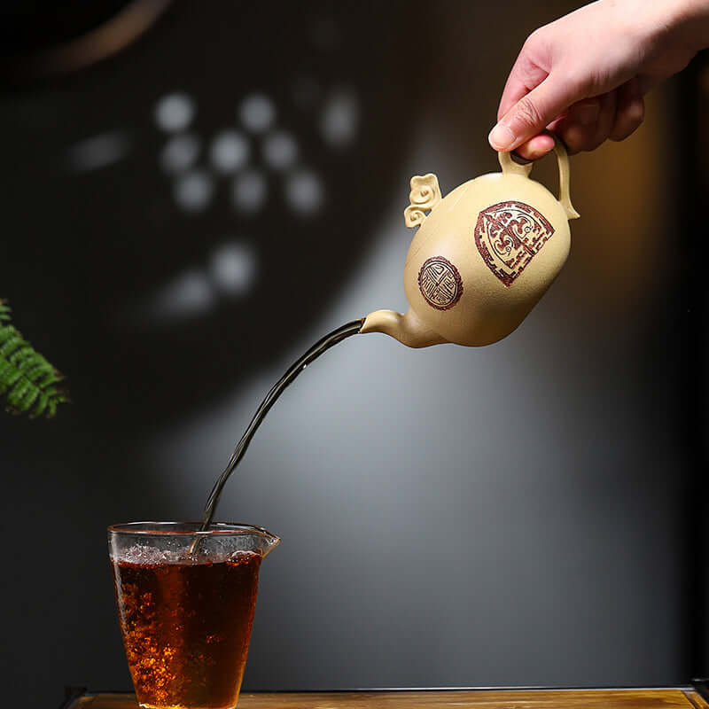 Handmade Yixing purple sand teapot pouring tea into a glass cup, showcasing elegant craftsmanship and traditional design.