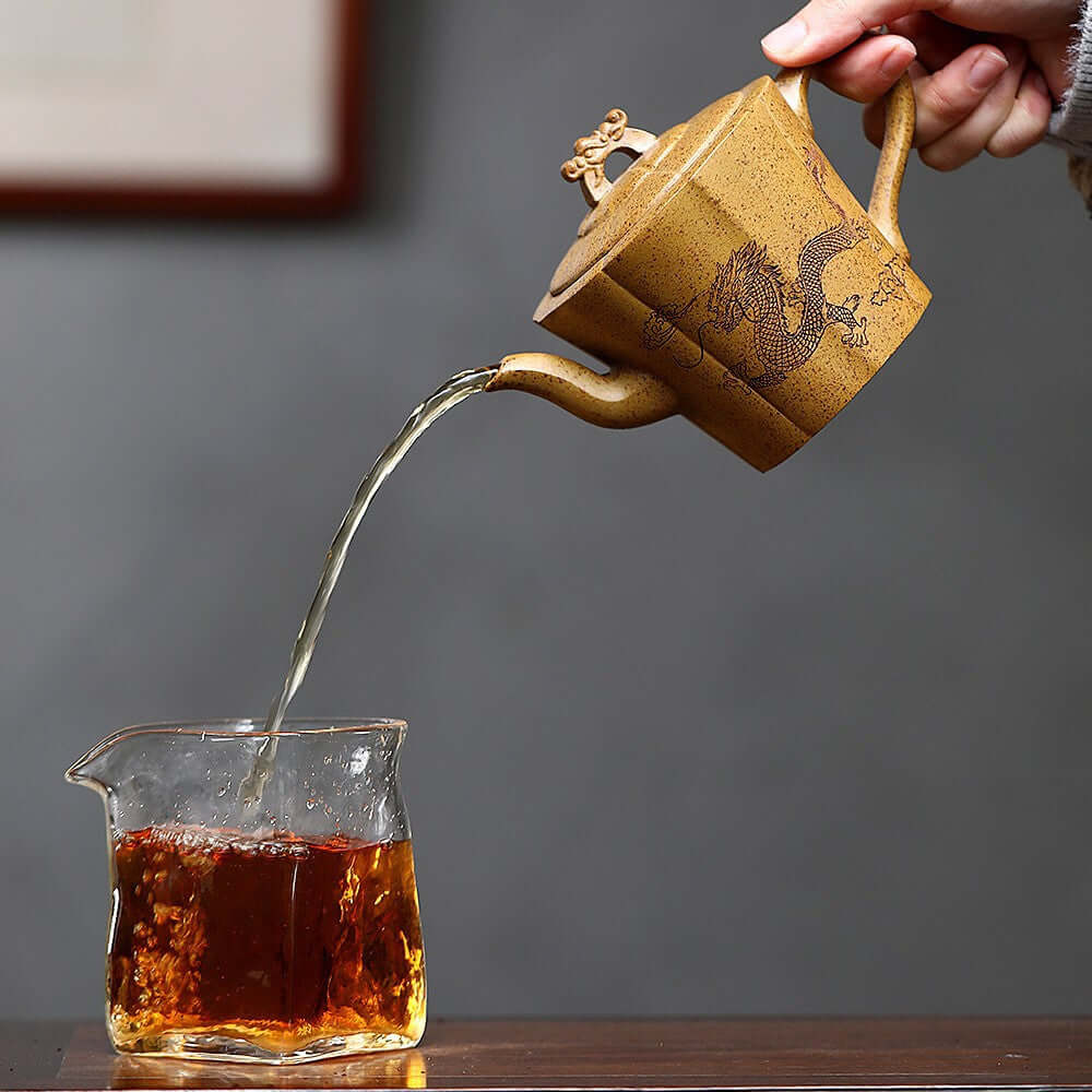 Handmade Yixing purple sand teapot pouring tea into a glass cup, showcasing artisan craftsmanship and traditional tea culture.