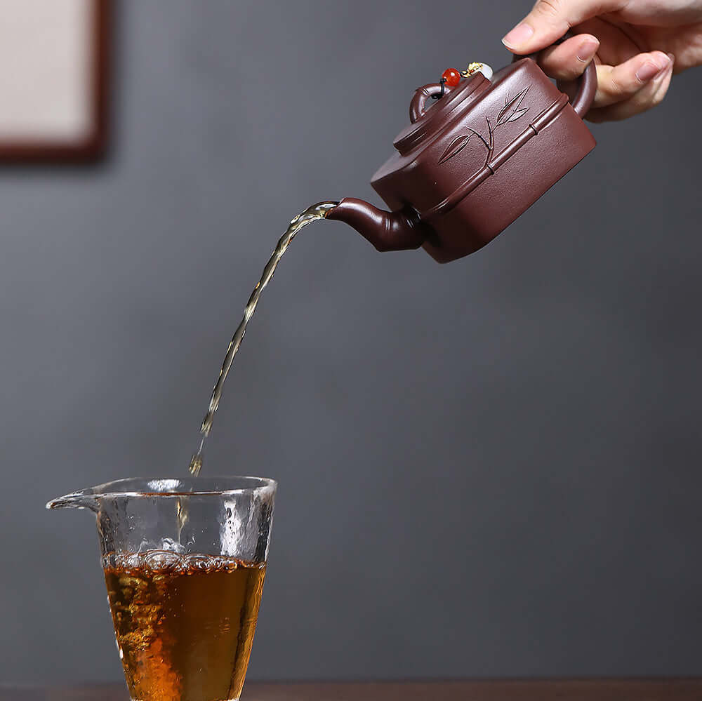 Handmade Yixing purple sand teapot pouring tea into a glass cup, showcasing the artistry of Kung Fu tea sets.
