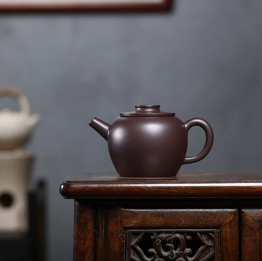 Handmade Yixing purple sand teapot on wooden table, showcasing original craftsmanship and elegant design.