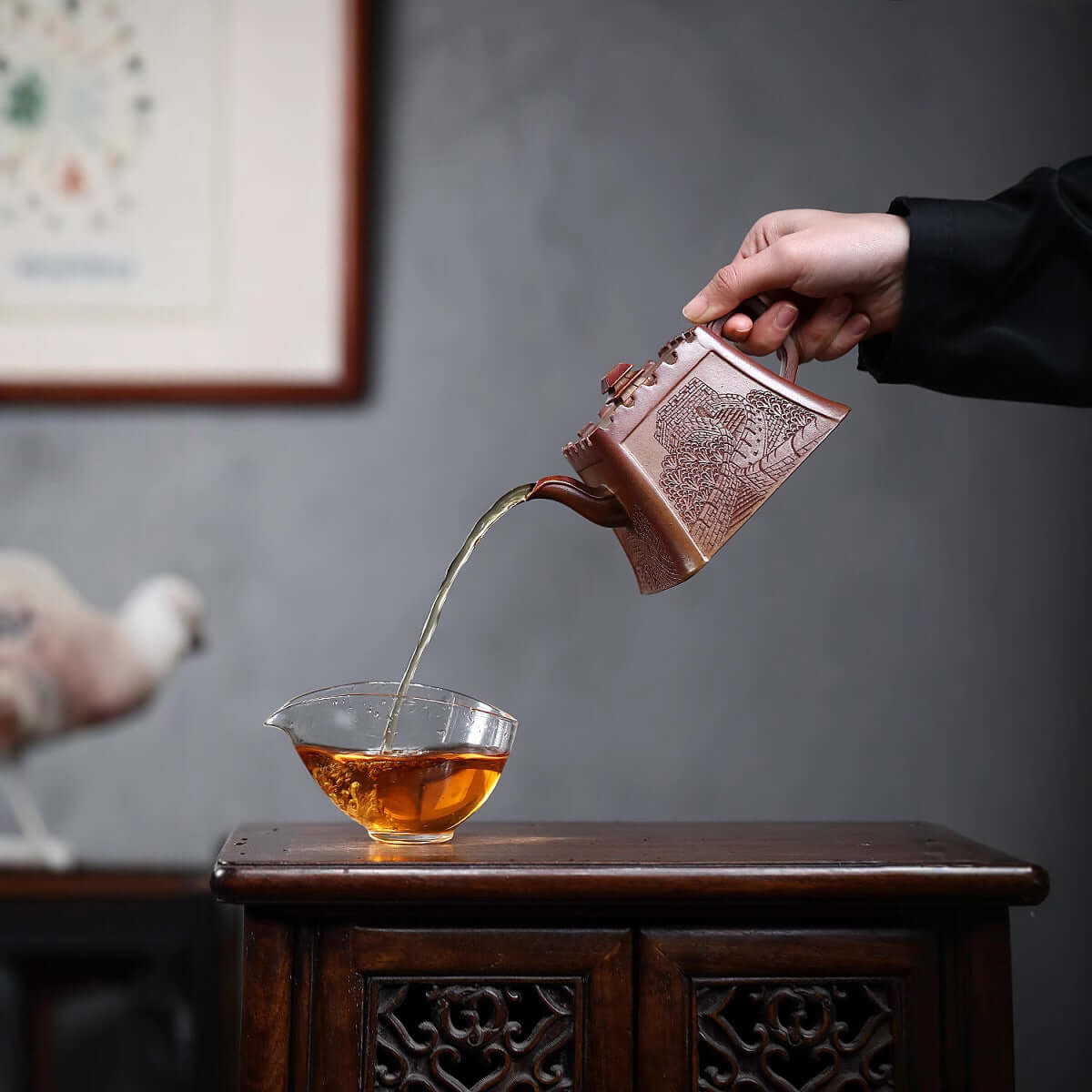 Handmade Yixing purple sand teapot pouring tea into a glass, showcasing traditional craftsmanship and rich design.