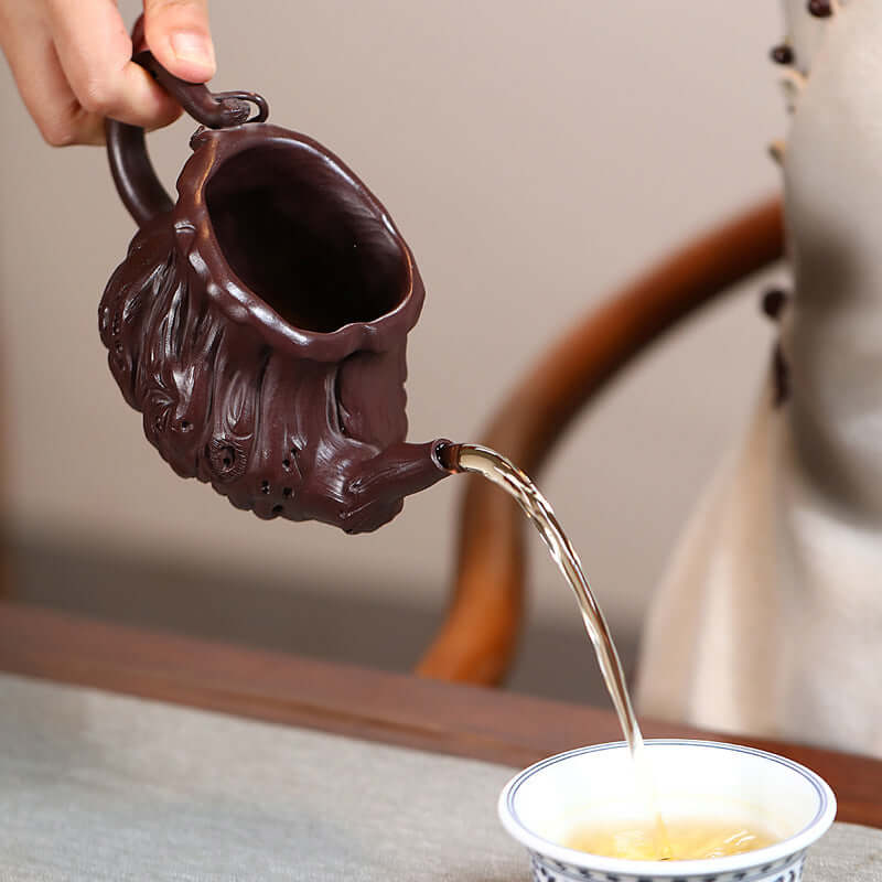 Handmade Yixing purple sand teapot pouring tea into a traditional tea cup, showcasing unique craftsmanship.