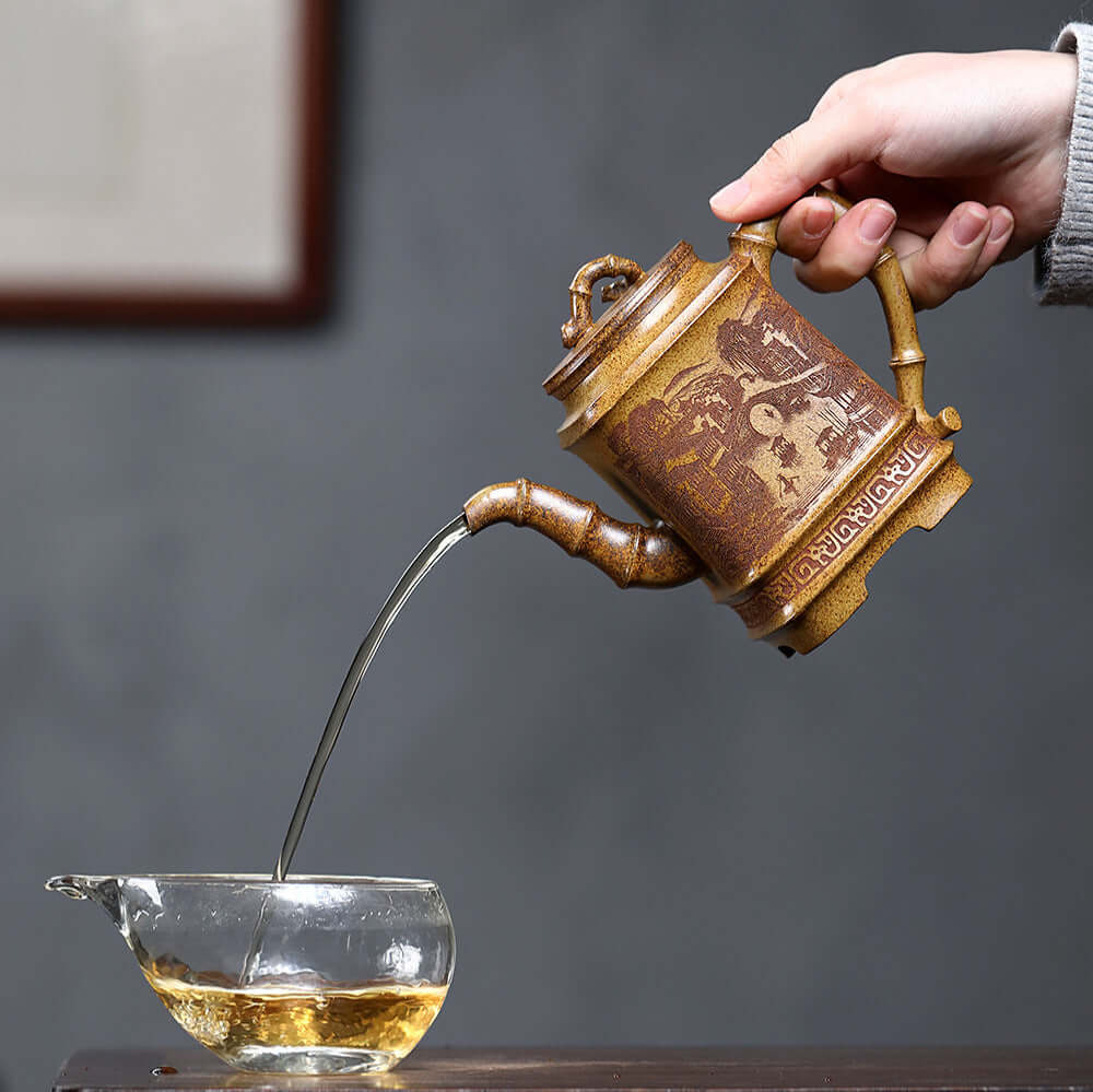 Handmade Yixing purple sand teapot pouring tea into a glass cup, showcasing traditional craftsmanship and elegant design.
