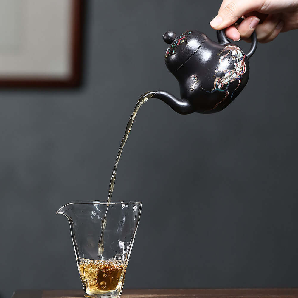 Handmade Yixing purple sand teapot pouring tea into a glass cup, showcasing craftsmanship and elegance in kung fu tea set.