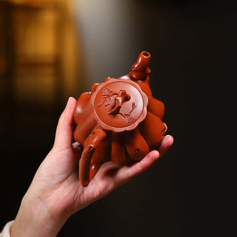 Handmade Yixing purple sand teapot held in hand, featuring intricate design and dark red clay texture.