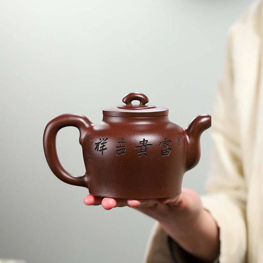 Handmade Yixing purple sand teapot held in hand, featuring elegant design and engraved characters.