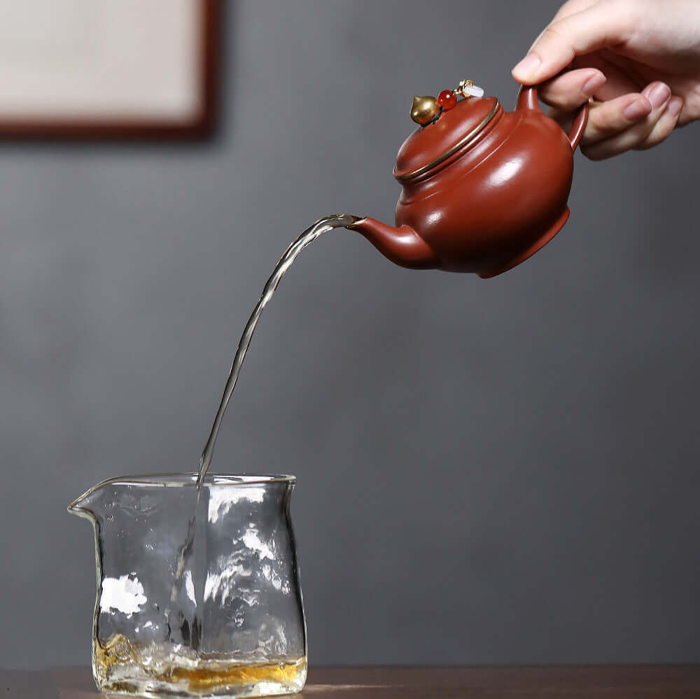 Handmade Yixing purple sand teapot with gold inlay pouring tea into a glass cup, perfect for Kung Fu tea sets.