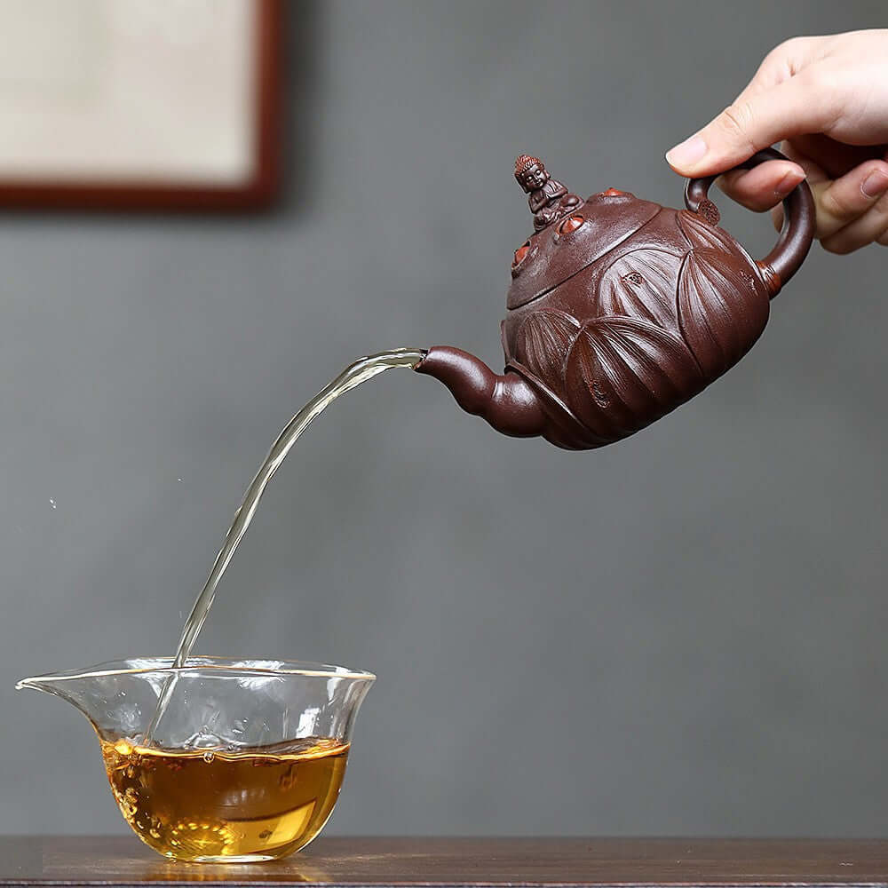 Handmade Yixing purple sand teapot pouring tea into a glass cup, showcasing detailed craftsmanship and elegant design.