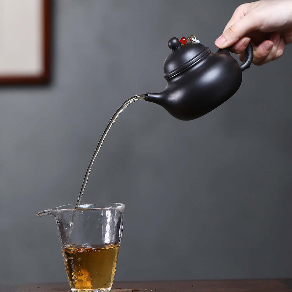 Handmade Yixing purple sand teapot pouring tea into a glass, showcasing original craftsmanship and elegant design.